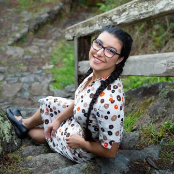 A woman sitting on outdoor steps wearing black-rimmed glasses and braids.