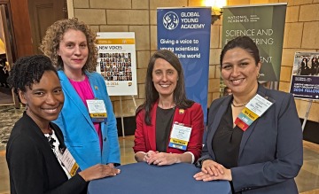 Four people smiling at a table with conference banners in the background.