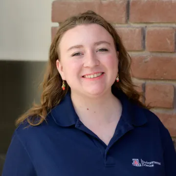 Smiling student with blue shirt in front of brick wall