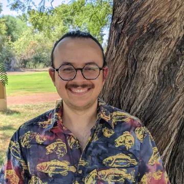 Smiling student with glasses in front of tree