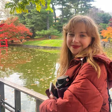 Smiling student with red jacket in front of body of water