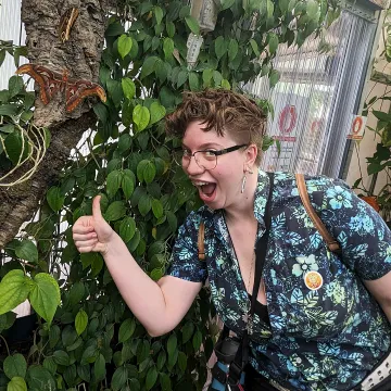 Smiling student with thumbs up in front of leaves