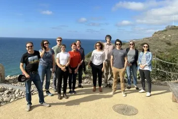 A group of people facing the camera on a bluff with the ocean behind them.