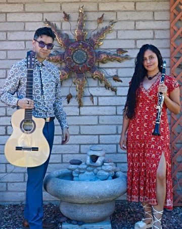 A man with a guitar stands next to a woman with a clarinet.