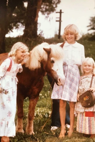 Three young girls smiling in dresses with a pony.
