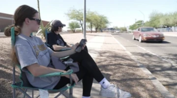 Two people sitting on foldable chairs on the sidewalk