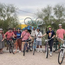 A group of people with bicycles stand outdoors smiling.